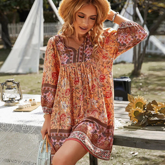 Women's lightweight mini dress featuring a warm-toned floral border print, split tie neckline, and long blouson sleeves in a relaxed babydoll silhouette.