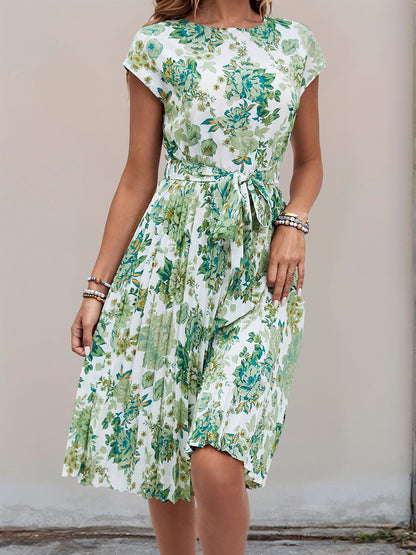 Green - Woman wearing a lightweight floral cap sleeve midi dress with a tie waist and pleated skirt.