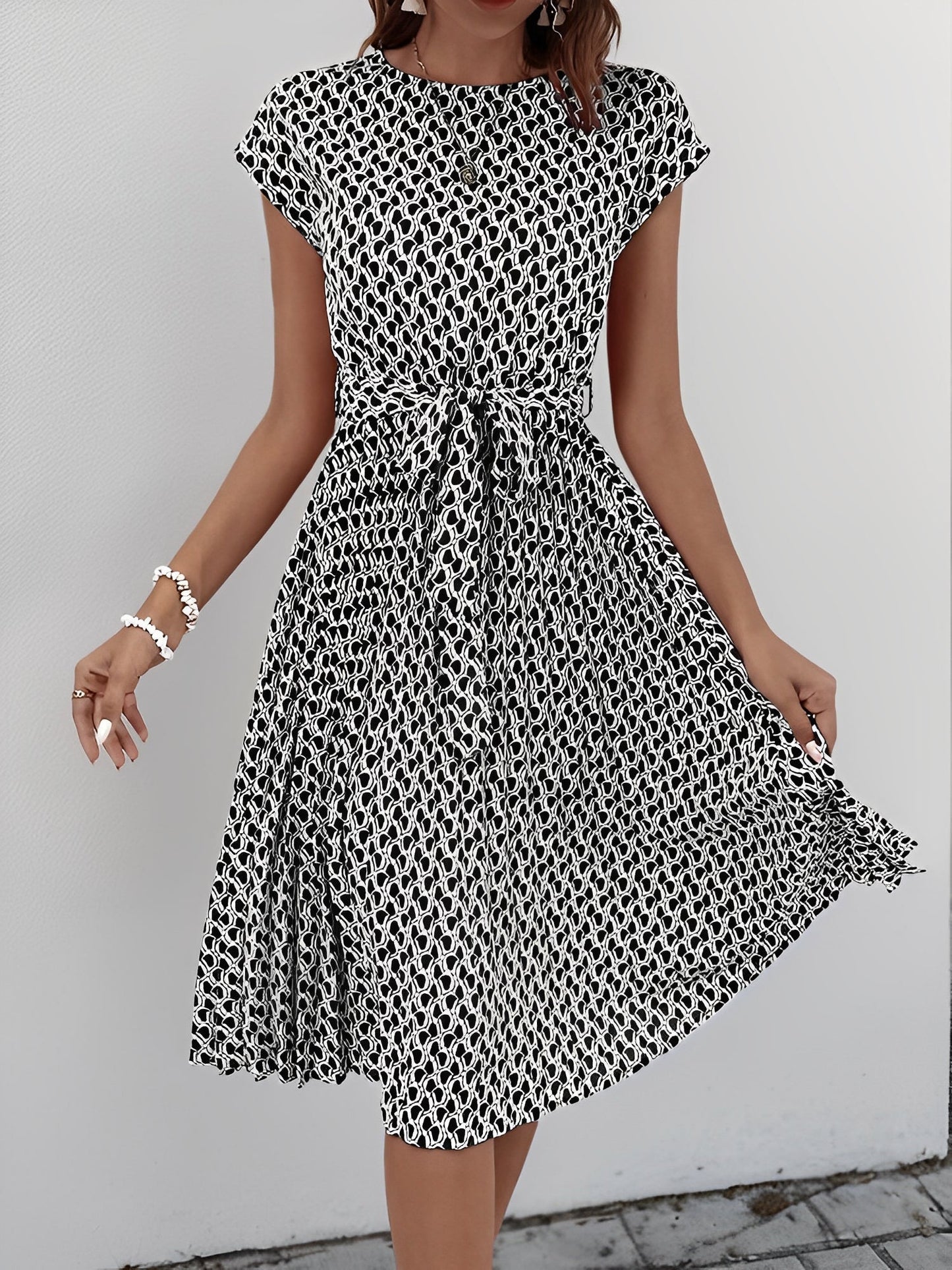 Black - Woman wearing a lightweight floral cap sleeve midi dress with a tie waist and pleated skirt.