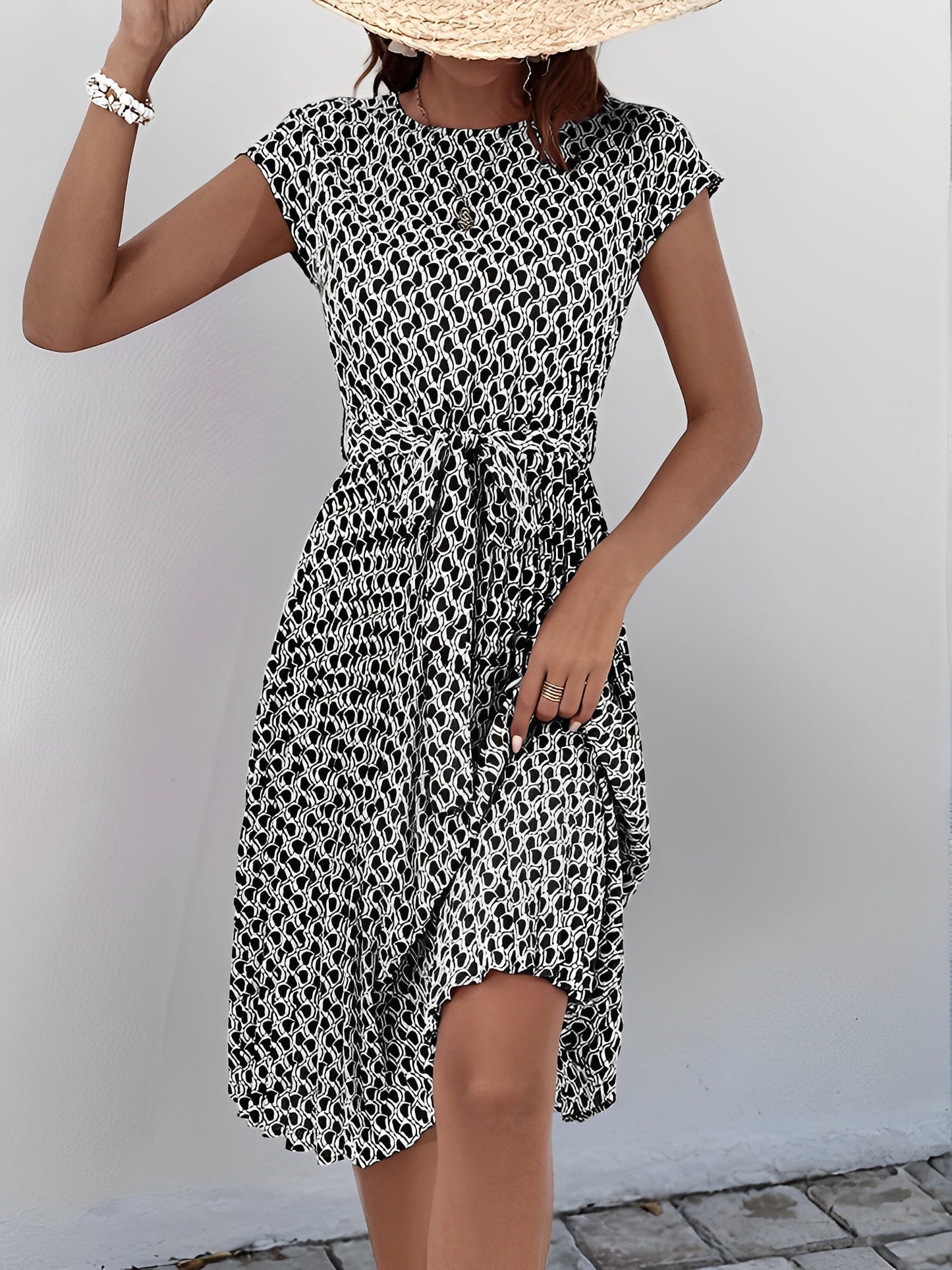 Black - Woman wearing a lightweight floral cap sleeve midi dress with a tie waist and pleated skirt.