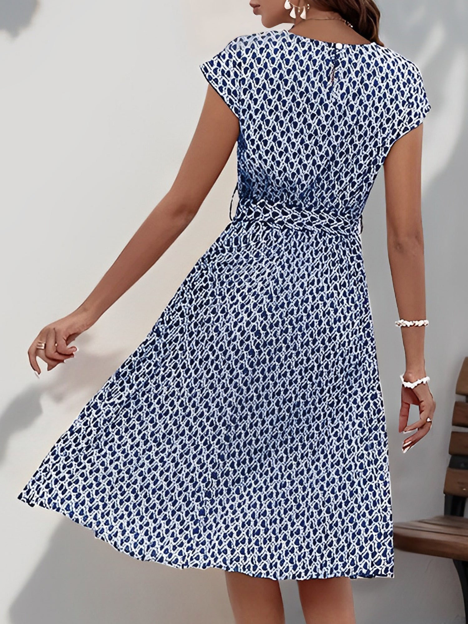 Navy Blue - Woman wearing a lightweight floral cap sleeve midi dress with a tie waist and pleated skirt.
