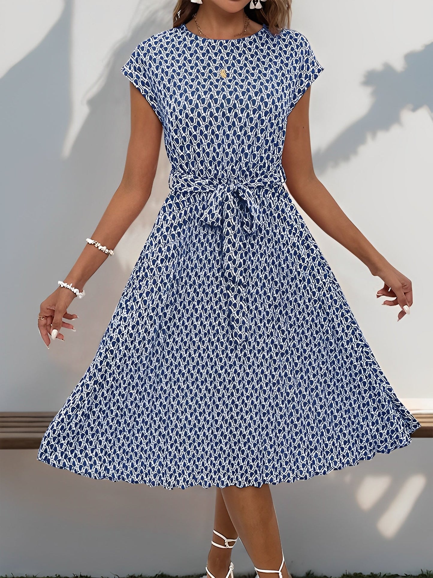 Navy Blue - Woman wearing a lightweight floral cap sleeve midi dress with a tie waist and pleated skirt.