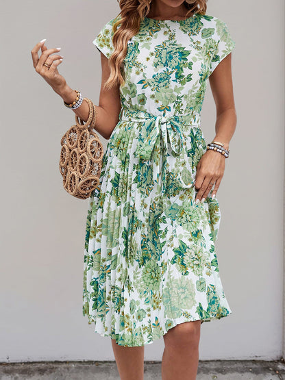Green - Woman wearing a lightweight floral cap sleeve midi dress with a tie waist and pleated skirt.