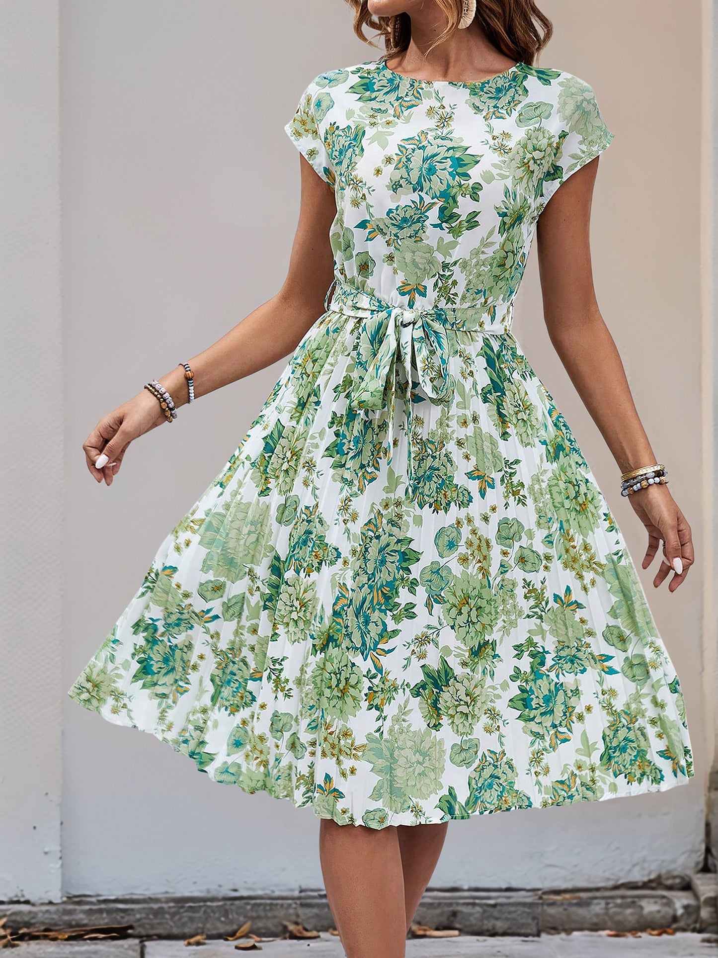 Green - Woman wearing a lightweight floral cap sleeve midi dress with a tie waist and pleated skirt.