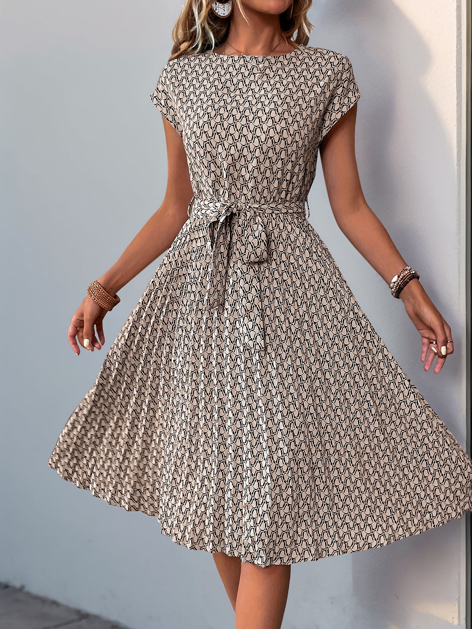 Khaki - Woman wearing a lightweight floral cap sleeve midi dress with a tie waist and pleated skirt.