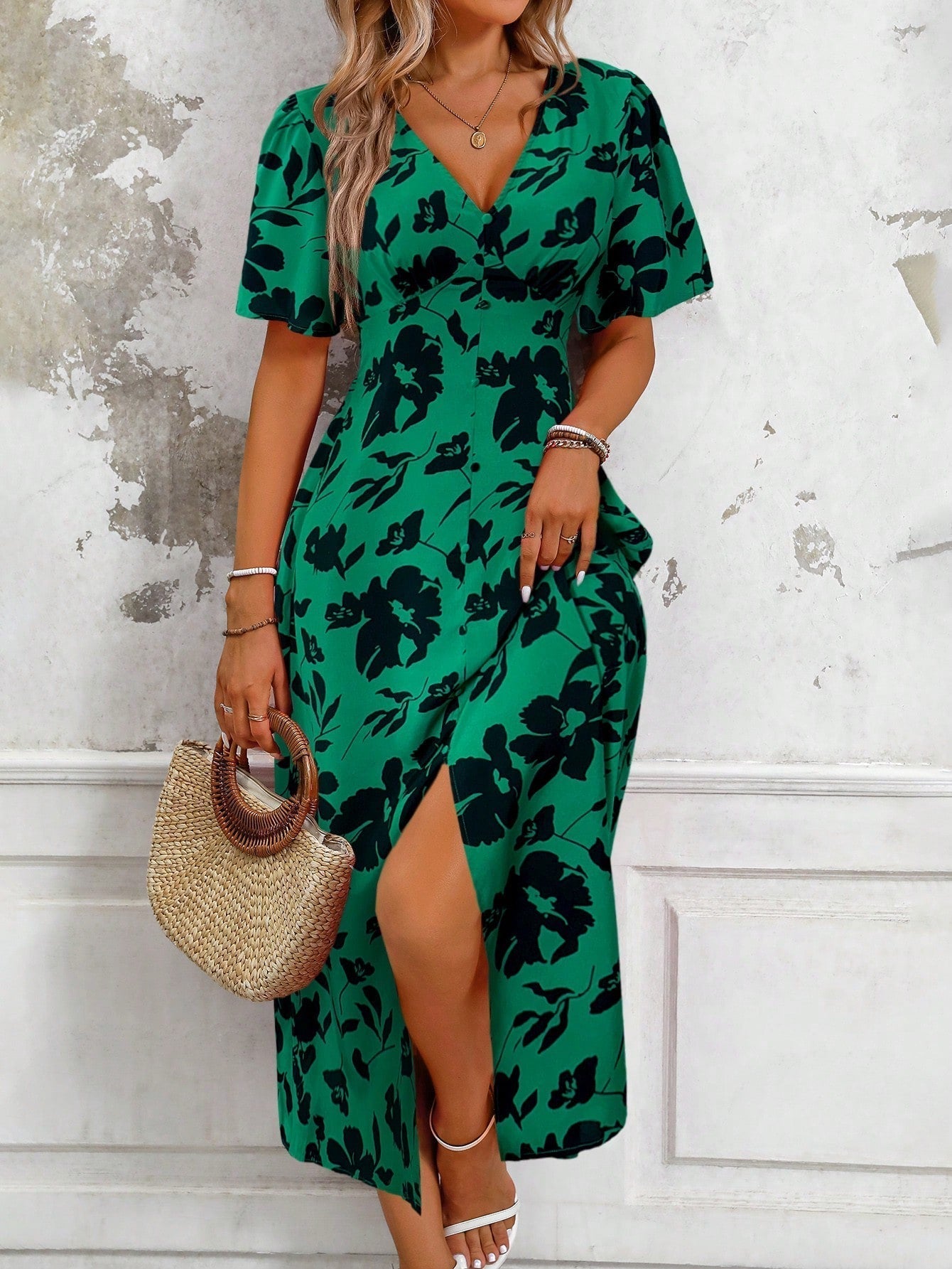 Blue - A woman wearing a pink and red floral print maxi dress with flutter sleeves, a V-neckline, button-front detailing, and a high front slit, holding a woven straw handbag.