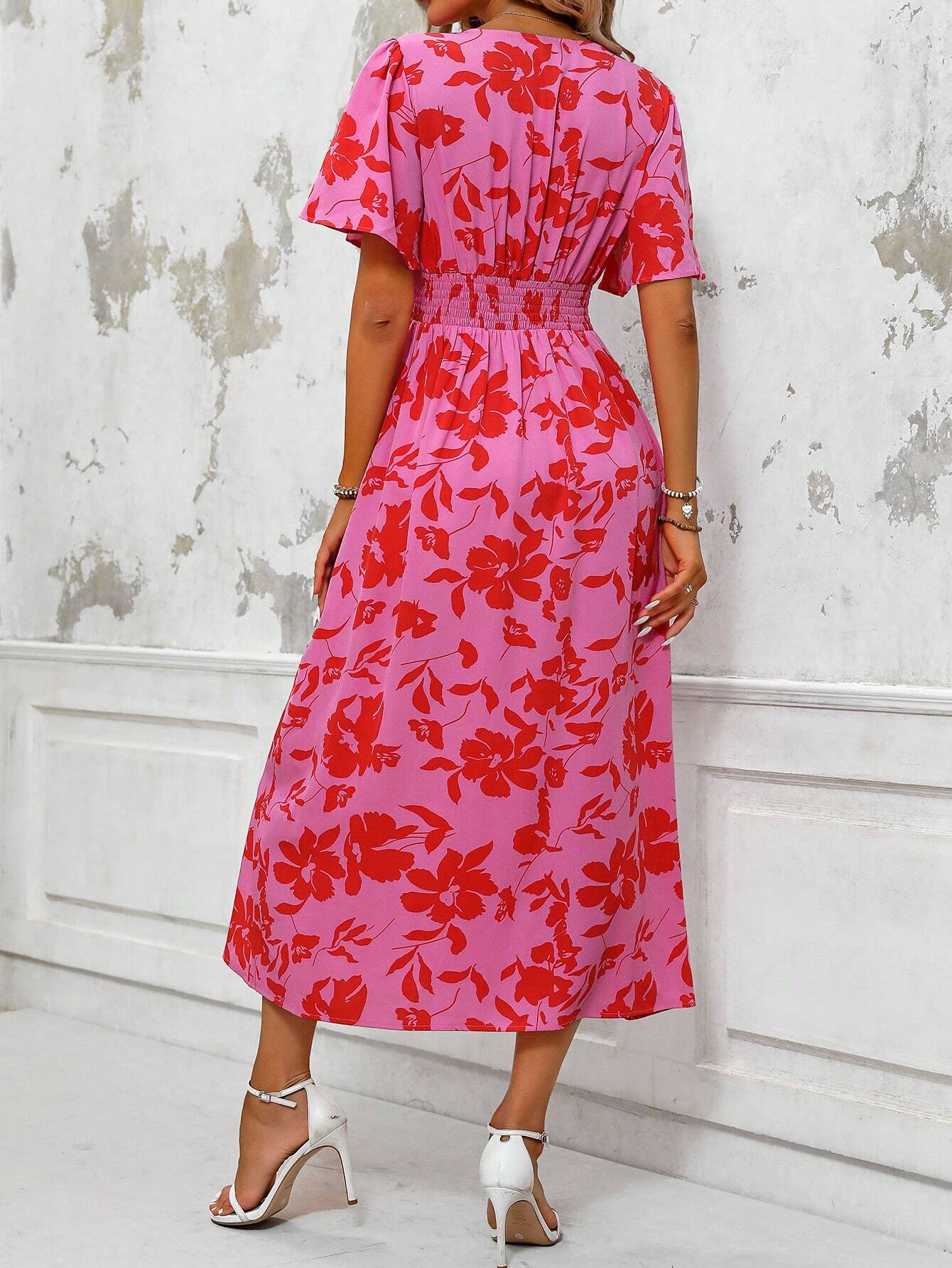 Pink - A woman wearing a pink and red floral print maxi dress with flutter sleeves, a V-neckline, button-front detailing, and a high front slit, holding a woven straw handbag.