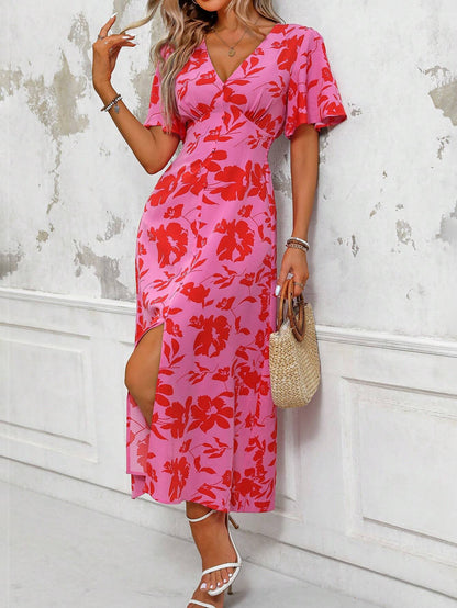 Pink - A woman wearing a pink and red floral print maxi dress with flutter sleeves, a V-neckline, button-front detailing, and a high front slit, holding a woven straw handbag.
