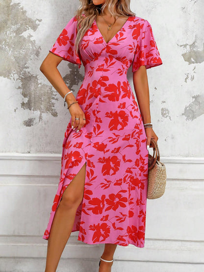 Pink - A woman wearing a pink and red floral print maxi dress with flutter sleeves, a V-neckline, button-front detailing, and a high front slit, holding a woven straw handbag.