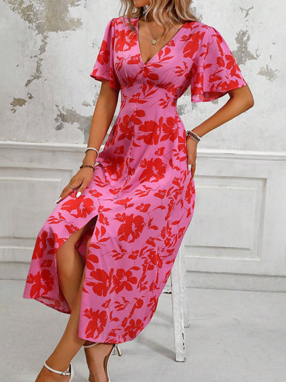 Pink - A woman wearing a pink and red floral print maxi dress with flutter sleeves, a V-neckline, button-front detailing, and a high front slit, holding a woven straw handbag.
