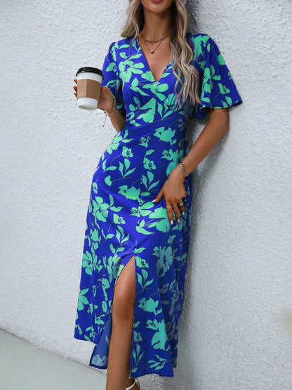 Blue - A woman wearing a pink and red floral print maxi dress with flutter sleeves, a V-neckline, button-front detailing, and a high front slit, holding a woven straw handbag.