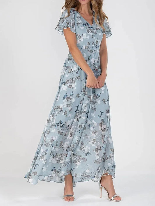 Light Blue - A woman wearing a dusty blue floral print chiffon maxi dress with flutter sleeves, a V-neckline, and a flowing skirt, paired with silver heeled sandals.