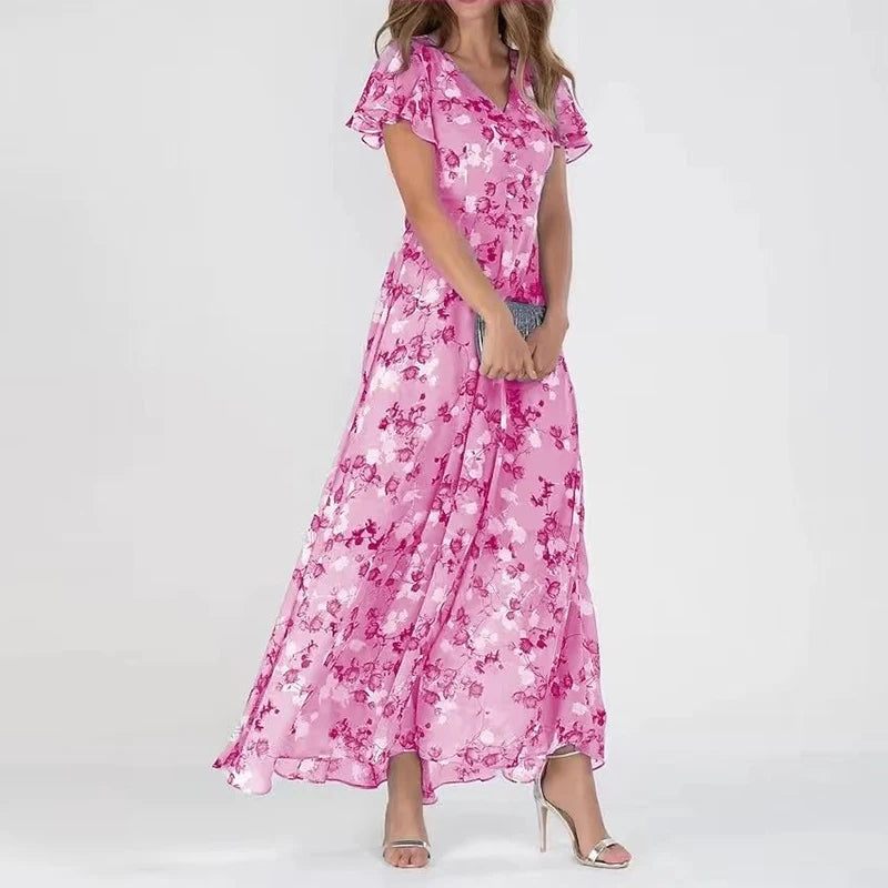 Pink - A woman wearing a dusty blue floral print chiffon maxi dress with flutter sleeves, a V-neckline, and a flowing skirt, paired with silver heeled sandals.