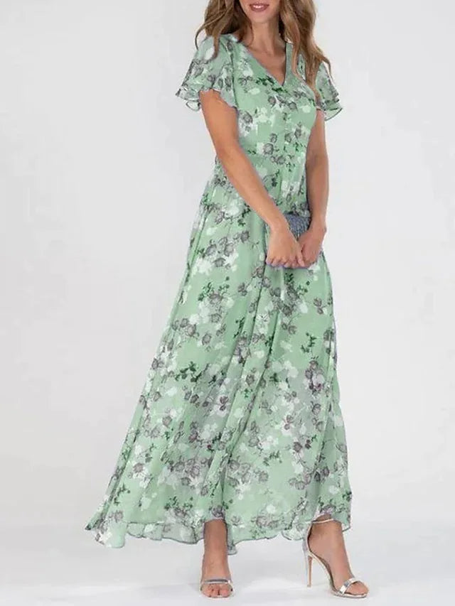 Green - A woman wearing a dusty blue floral print chiffon maxi dress with flutter sleeves, a V-neckline, and a flowing skirt, paired with silver heeled sandals.