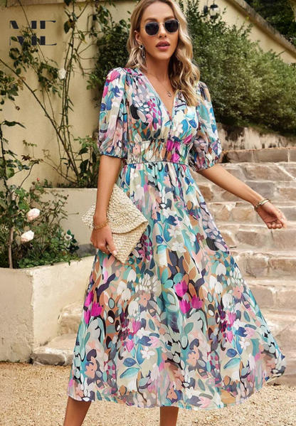 Light Blue - Woman wearing a multicolored abstract floral chiffon midi dress with a V-neckline, elbow-length puff sleeves, and a smocked waist, standing outdoors on stone steps.