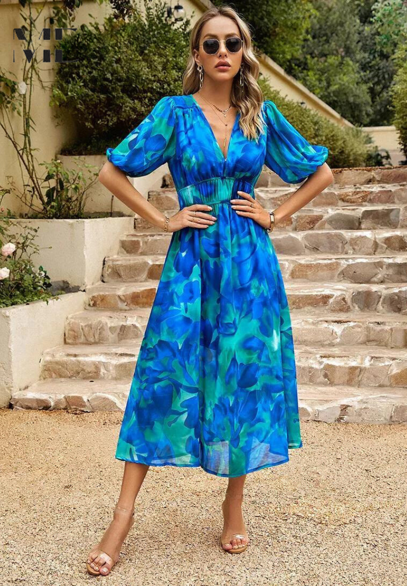 Blue - Woman wearing a multicolored abstract floral chiffon midi dress with a V-neckline, elbow-length puff sleeves, and a smocked waist, standing outdoors on stone steps.
