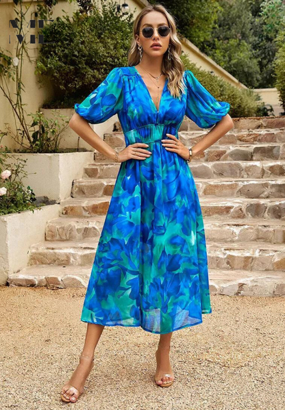 Blue - Woman wearing a multicolored abstract floral chiffon midi dress with a V-neckline, elbow-length puff sleeves, and a smocked waist, standing outdoors on stone steps.