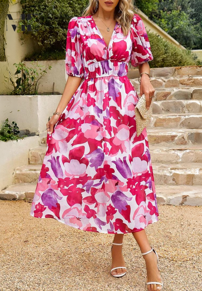 Pink - Woman wearing a multicolored abstract floral chiffon midi dress with a V-neckline, elbow-length puff sleeves, and a smocked waist, standing outdoors on stone steps.