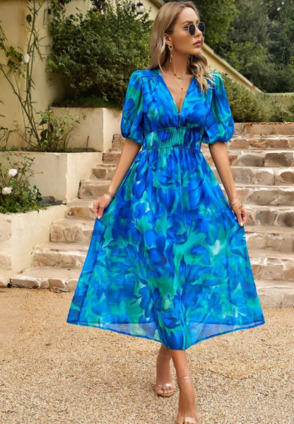 Pink - Woman wearing a multicolored abstract floral chiffon midi dress with a V-neckline, elbow-length puff sleeves, and a smocked waist, standing outdoors on stone steps.