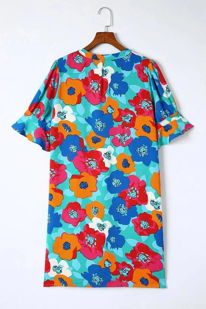 Orange - Woman wearing a vibrant teal mini shift dress with large abstract pink, orange, and blue floral print, featuring a split neckline and flutter sleeves.