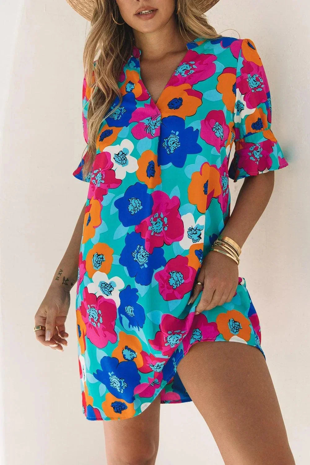 Blue - Woman wearing a vibrant teal mini shift dress with large abstract pink, orange, and blue floral print, featuring a split neckline and flutter sleeves.