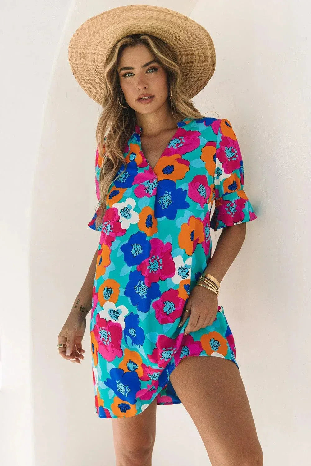 Blue - Woman wearing a vibrant teal mini shift dress with large abstract pink, orange, and blue floral print, featuring a split neckline and flutter sleeves.