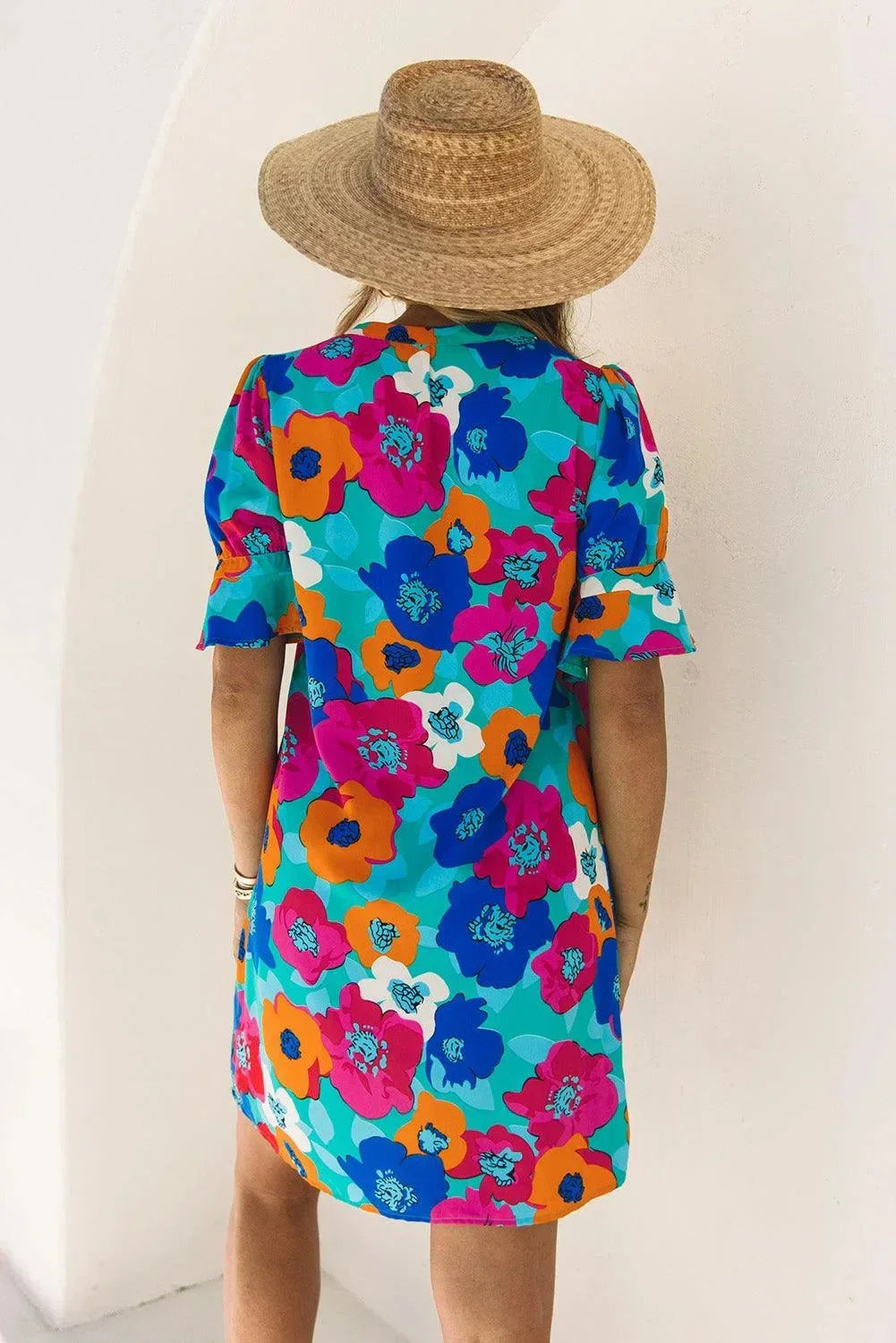 Blue - Woman wearing a vibrant teal mini shift dress with large abstract pink, orange, and blue floral print, featuring a split neckline and flutter sleeves.