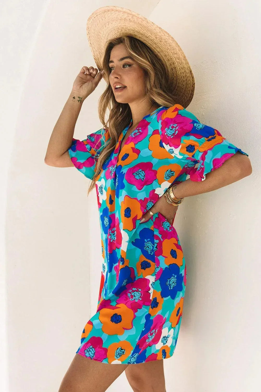 Blue - Woman wearing a vibrant teal mini shift dress with large abstract pink, orange, and blue floral print, featuring a split neckline and flutter sleeves.
