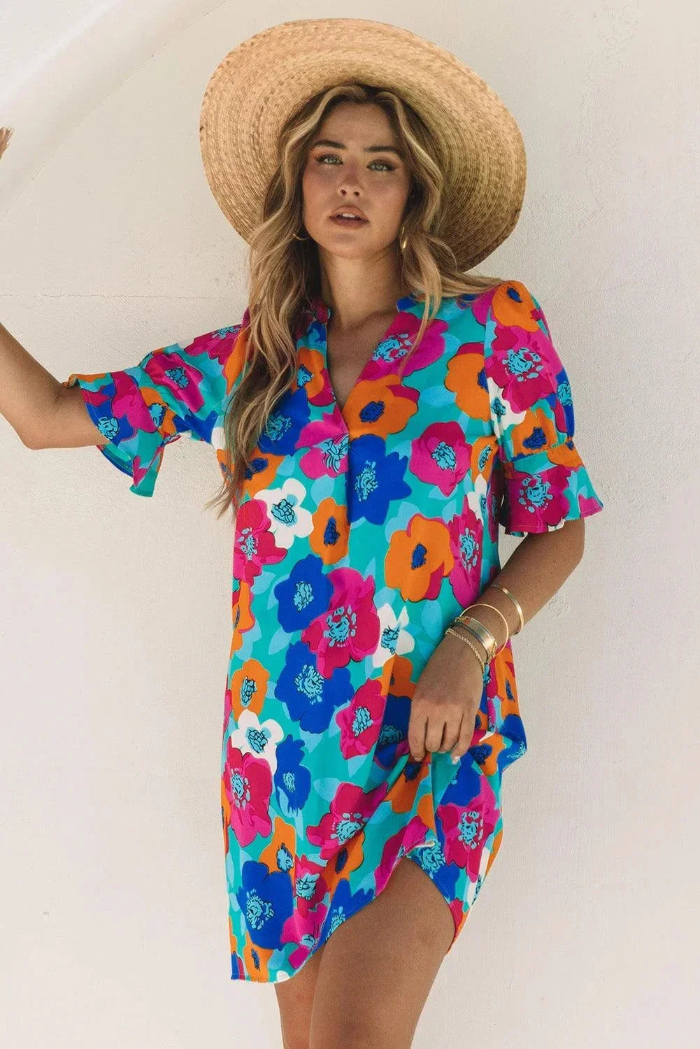 Blue - Woman wearing a vibrant teal mini shift dress with large abstract pink, orange, and blue floral print, featuring a split neckline and flutter sleeves.