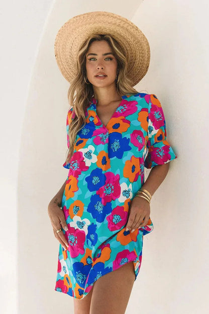 Blue - Woman wearing a vibrant teal mini shift dress with large abstract pink, orange, and blue floral print, featuring a split neckline and flutter sleeves.