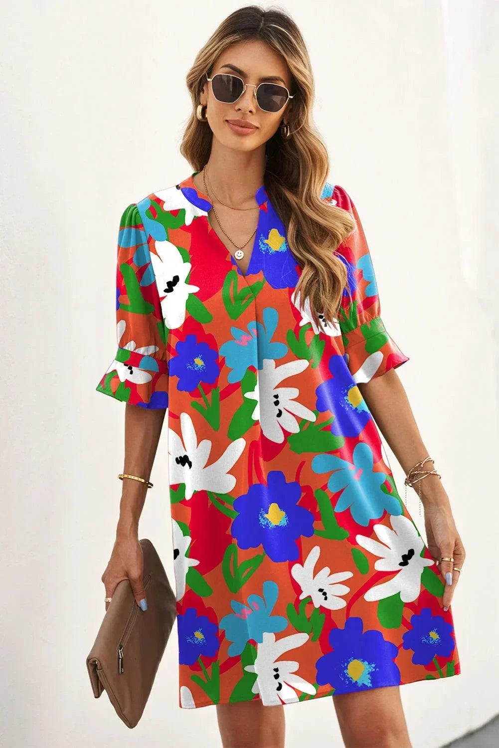 Orange - Woman wearing a vibrant teal mini shift dress with large abstract pink, orange, and blue floral print, featuring a split neckline and flutter sleeves.