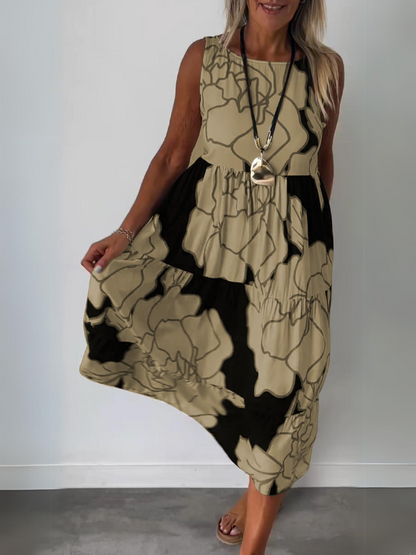 Brown - A woman wearing a sleeveless, tiered midi dress featuring a large-scale black and white floral outline print with tan accents, styled with a gold pendant necklace.