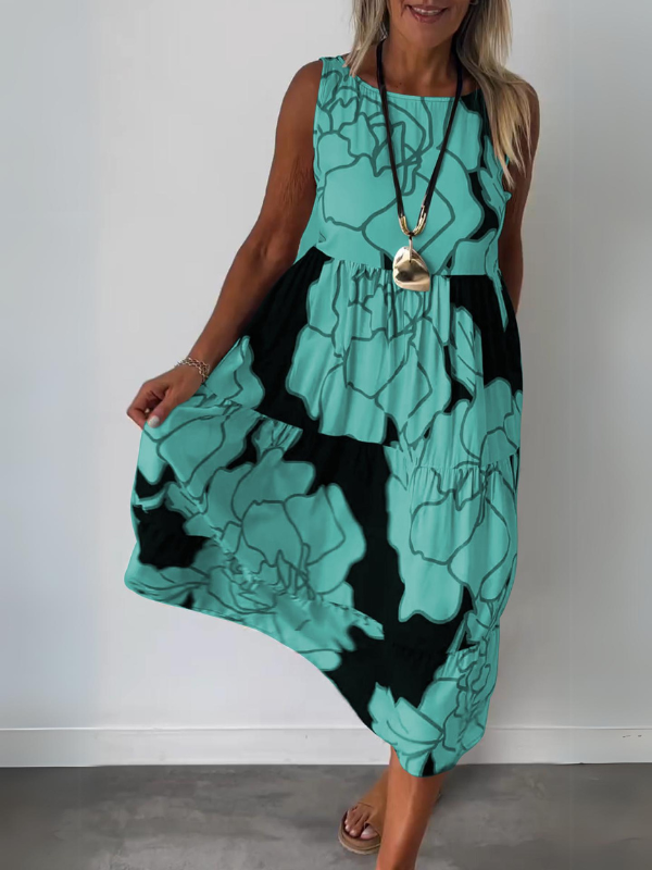 Green - A woman wearing a sleeveless, tiered midi dress featuring a large-scale black and white floral outline print with tan accents, styled with a gold pendant necklace.