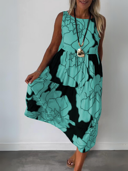 Green - A woman wearing a sleeveless, tiered midi dress featuring a large-scale black and white floral outline print with tan accents, styled with a gold pendant necklace.