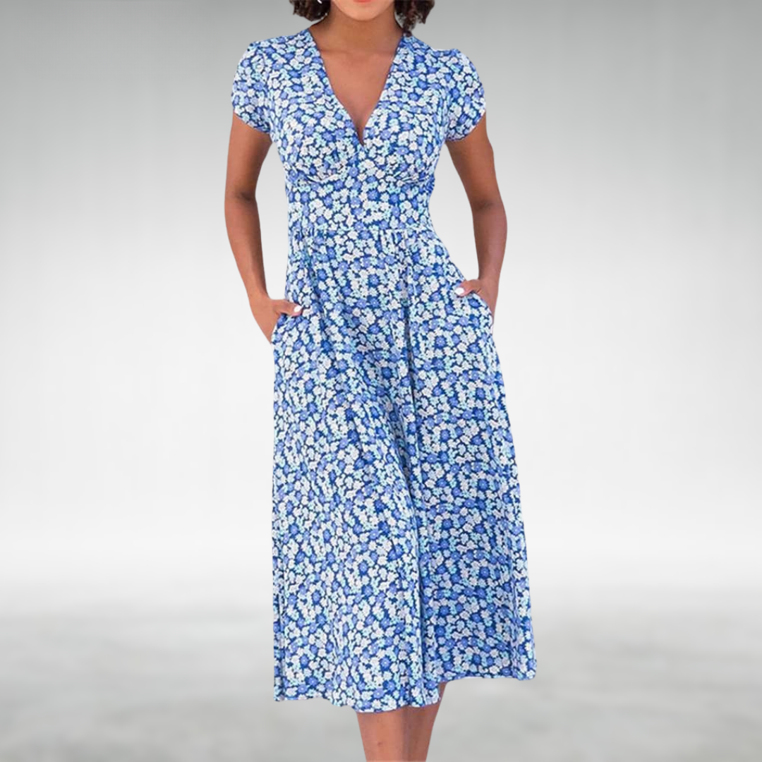 Blue - A woman wearing a blue and white ditsy floral print midi dress featuring a V-neckline, short cap sleeves, and side pockets, set against a neutral gray background.