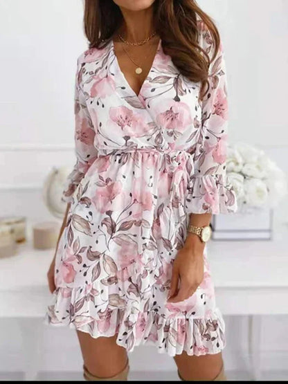 White - Woman wearing a white chiffon mini dress with pink floral print, featuring a wrap silhouette, ruffled hem, and three-quarter sleeves with ruffled cuffs.
