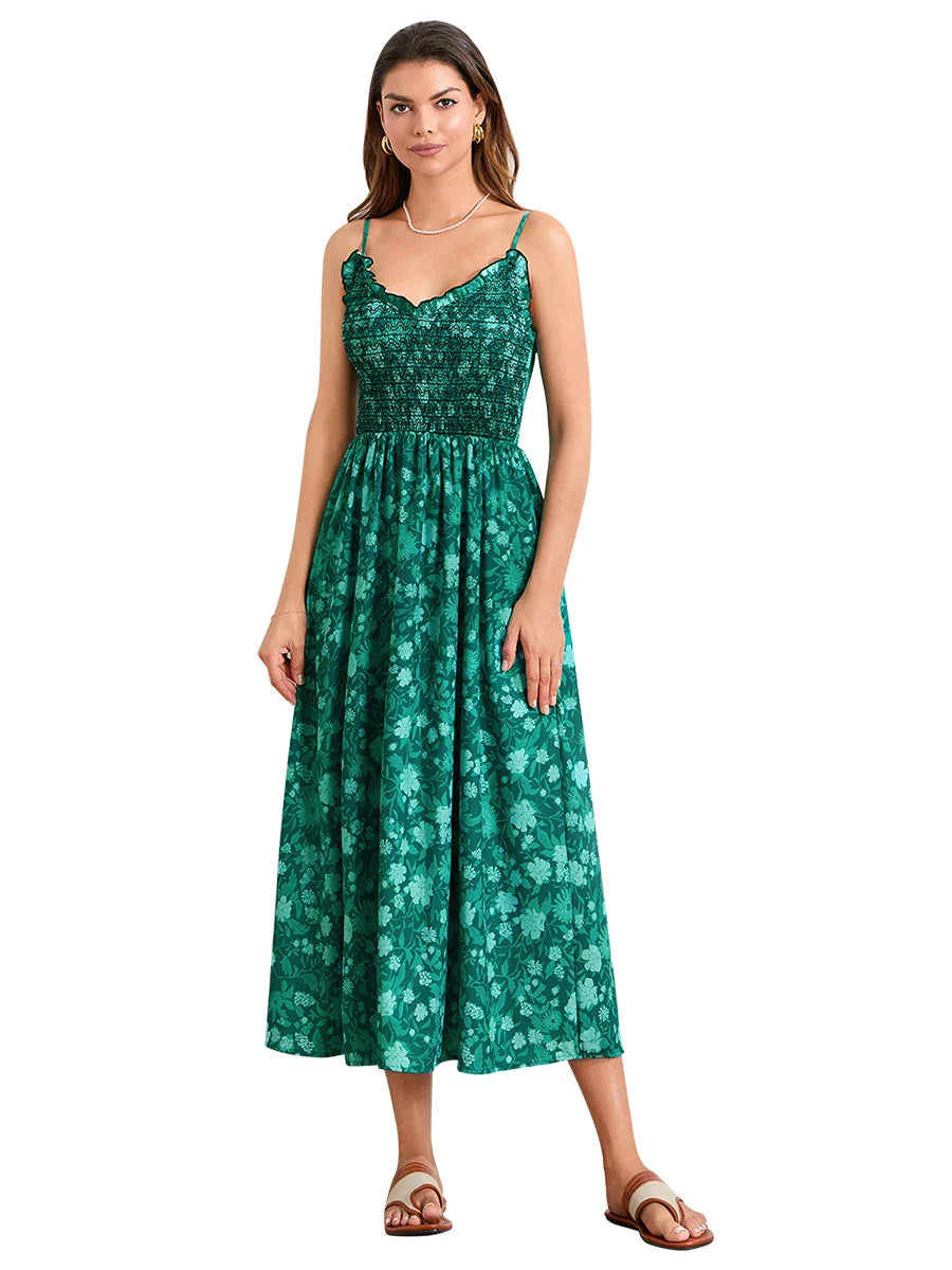 Floral Cyan - A woman wearing a pink and white floral print maxi dress featuring a smocked bodice, ruffled neckline, and thin straps, standing against a rustic stone wall.