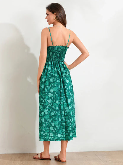 Floral Cyan - A woman wearing a pink and white floral print maxi dress featuring a smocked bodice, ruffled neckline, and thin straps, standing against a rustic stone wall.