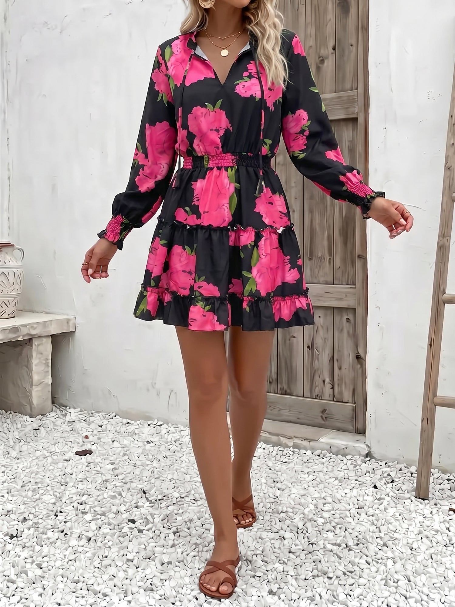 Rose Red - Woman wearing a dark mini dress with large bright floral print, featuring long sleeves, a smocked waist, and a tiered ruffle skirt