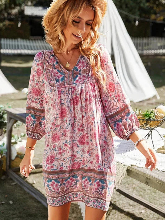 Pink bohemian floral print mini dress featuring a v-neckline with tie details, three-quarter blouson sleeves, and a relaxed shift silhouette with border print hem.