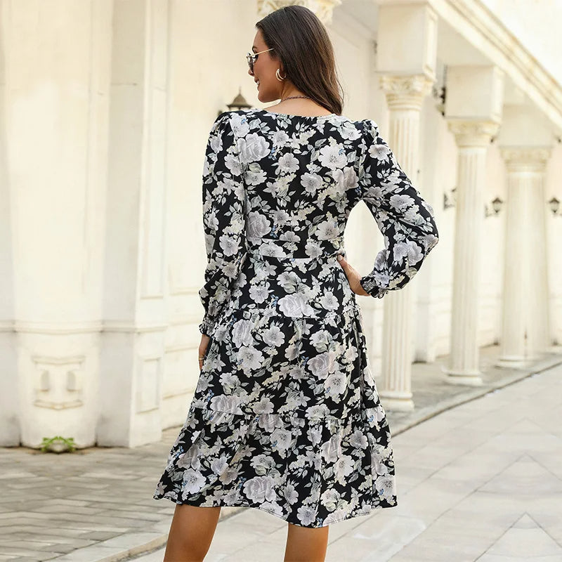 Black - Woman wearing a monochrome large-scale floral print midi dress featuring a V-neckline, button-front bodice, long sleeves, and a tiered skirt.
