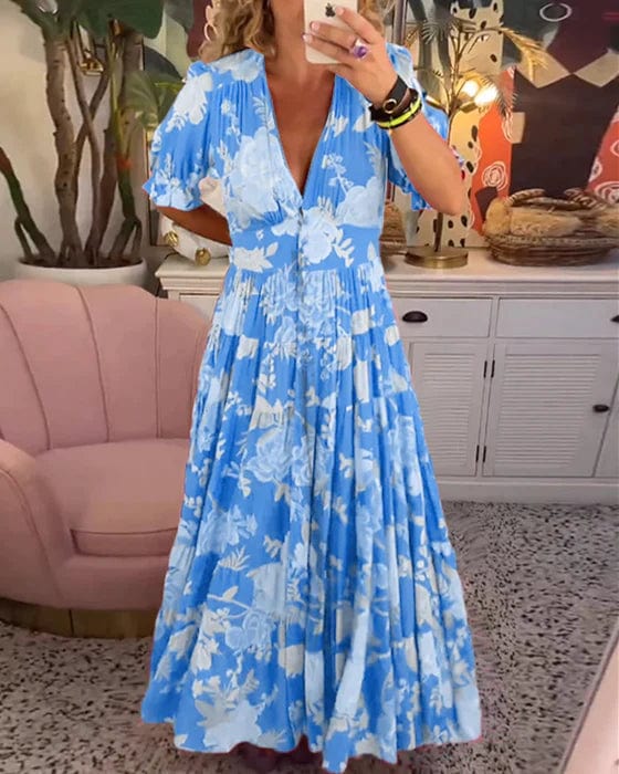 Blue - A woman wearing a vibrant pink maxi dress with a blue and light pink floral print, featuring a deep V-neckline, short puff sleeves, and a gathered, flowing skirt.