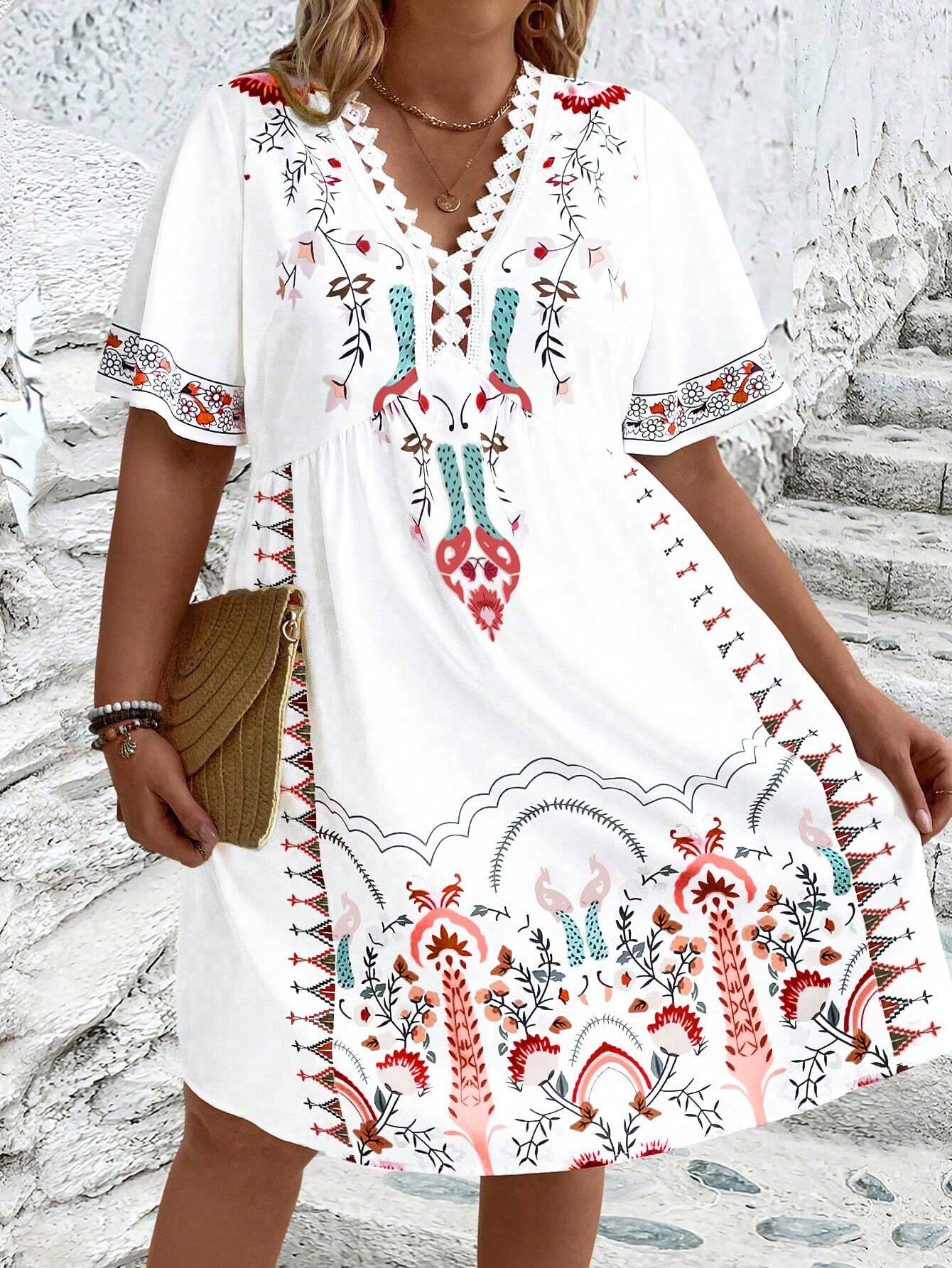 A woman wearing a white midi dress featuring a colorful folk-inspired floral print, a crochet-trimmed V-neckline, and short flutter sleeves, holding a woven straw clutch.