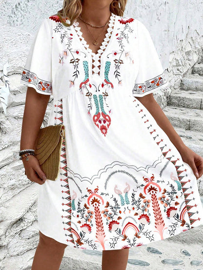A woman wearing a white midi dress featuring a colorful folk-inspired floral print, a crochet-trimmed V-neckline, and short flutter sleeves, holding a woven straw clutch.