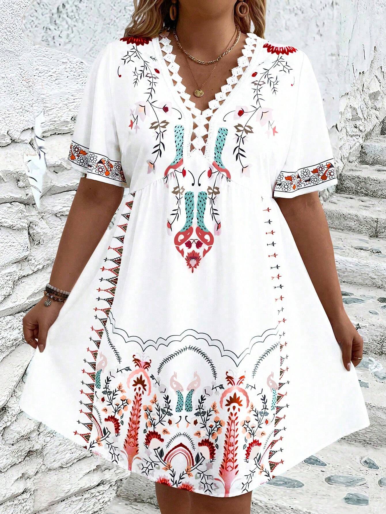 A woman wearing a white midi dress featuring a colorful folk-inspired floral print, a crochet-trimmed V-neckline, and short flutter sleeves, holding a woven straw clutch.