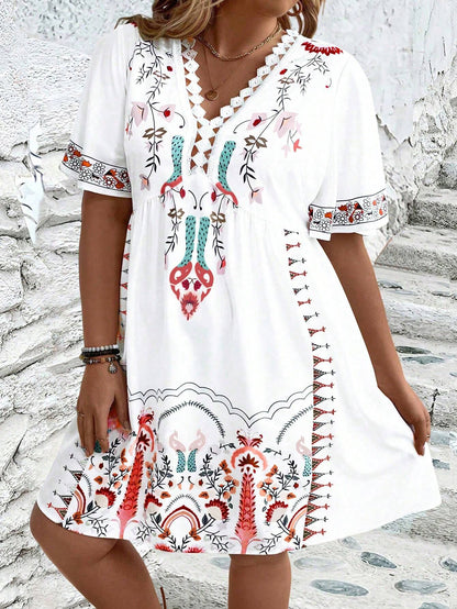 A woman wearing a white midi dress featuring a colorful folk-inspired floral print, a crochet-trimmed V-neckline, and short flutter sleeves, holding a woven straw clutch.