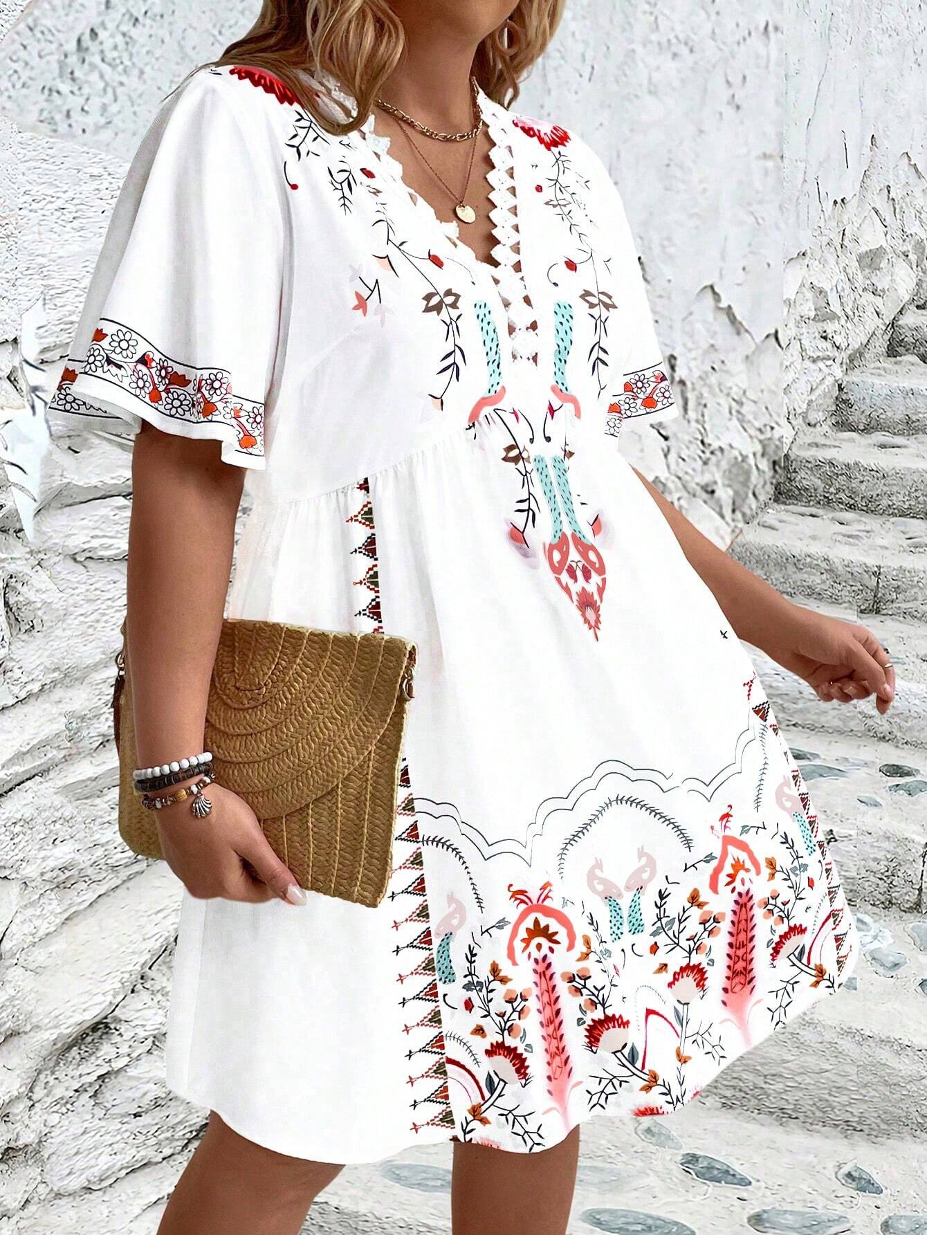 A woman wearing a white midi dress featuring a colorful folk-inspired floral print, a crochet-trimmed V-neckline, and short flutter sleeves, holding a woven straw clutch.
