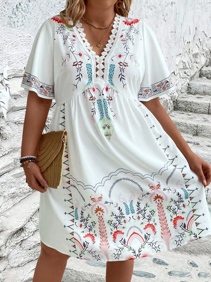 White - A woman wearing a white midi dress featuring a colorful folk-inspired floral print, a crochet-trimmed V-neckline, and short flutter sleeves, holding a woven straw clutch.