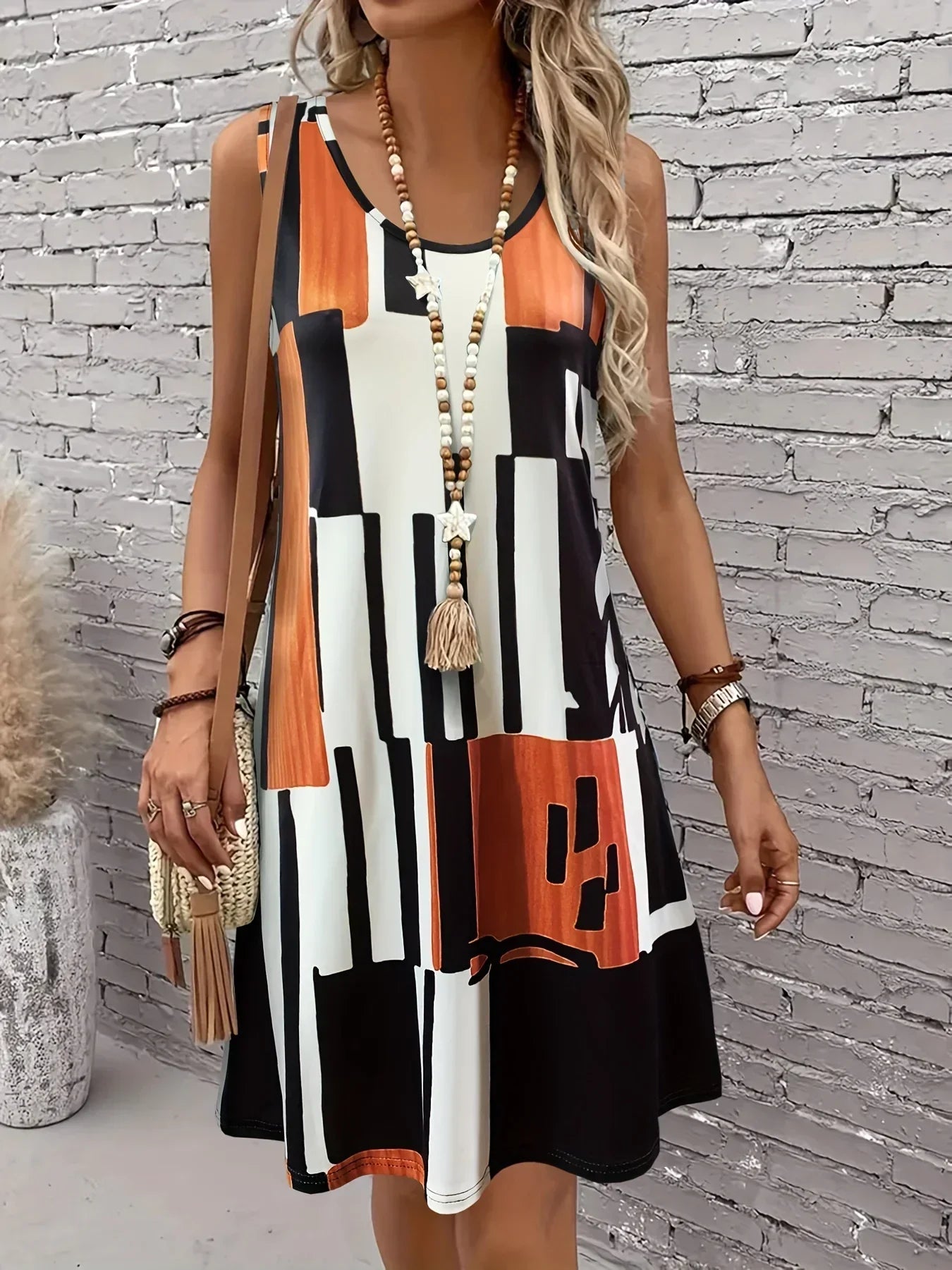 Light Brown - A woman wearing a sleeveless A-line shift dress featuring a bold black, white, and rust-orange geometric block print, styled with a bohemian wooden bead tassel necklace and a woven shoulder bag.