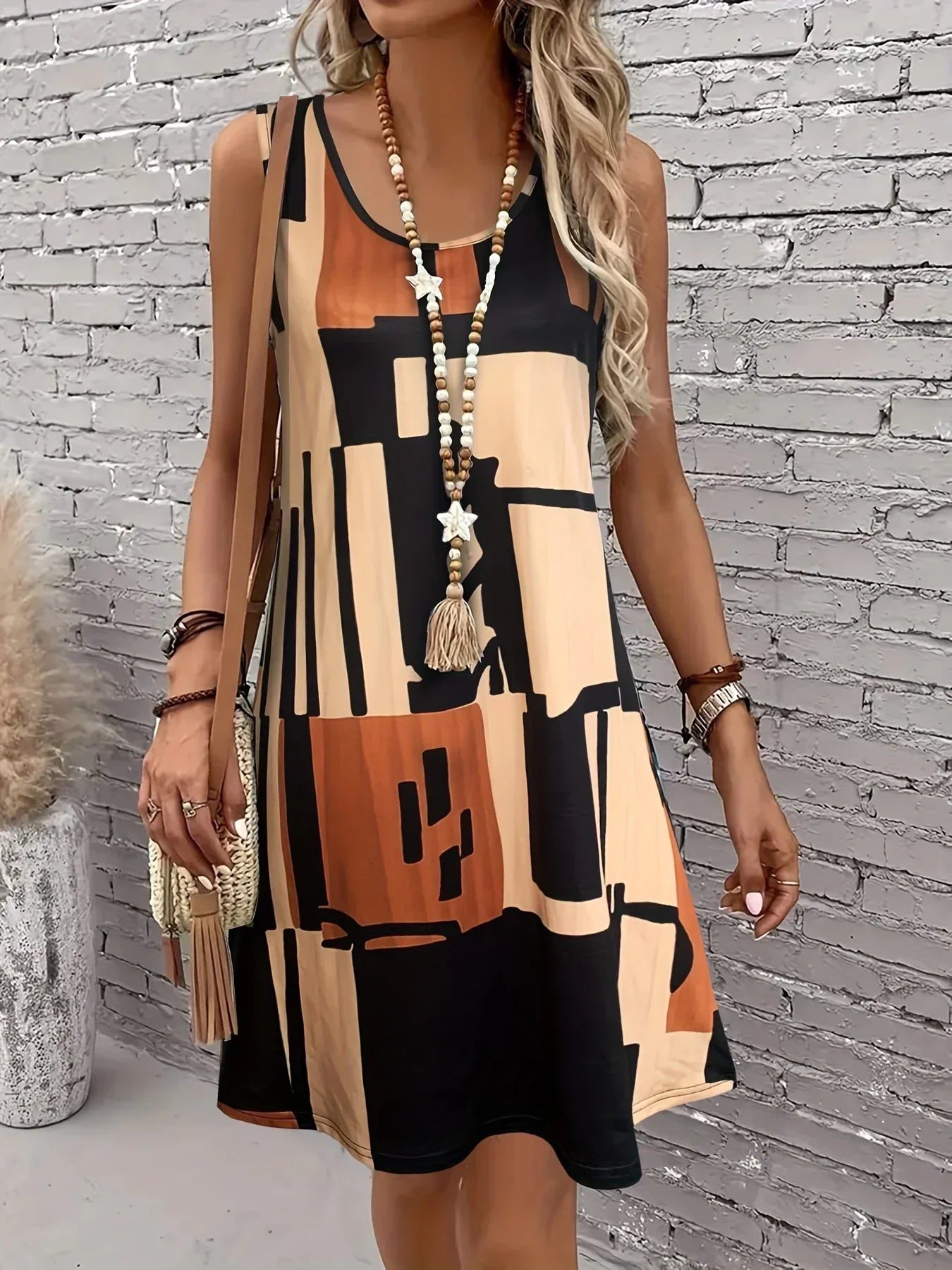 Chocolate - A woman wearing a sleeveless A-line shift dress featuring a bold black, white, and rust-orange geometric block print, styled with a bohemian wooden bead tassel necklace and a woven shoulder bag.